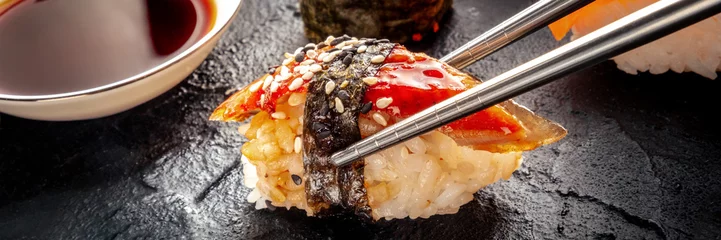 Tragetasche Sushi with chopsticks and soy sauce panorama. Unagi sushi, nigiri with eel, on a black background. Japanese restaurant © Ilya