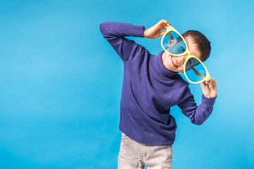 Fototapeta premium Cheerful little boy in big glasses express a surprised face isolated on blue background with copy space