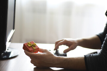 A man with a gift in his hand sits in front of the monitor screen. Order a gift for home and office.