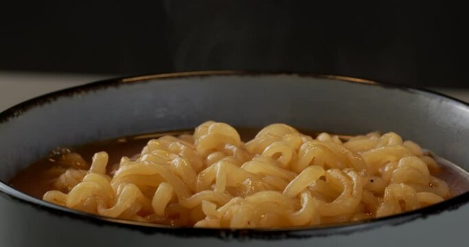 Korean spicy noodle soup ramyeon. The soup is poured into a bowl. Hot instant noodles are steaming in the bowl. Close-up footage on the rotating table.
