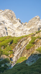 Waterfall on the hills of the  rocky and snowy mountains on a sunny day