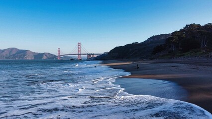 Scenic shot of foamy waves of Baker beach of San Francisco with Golden gate bridge on the background