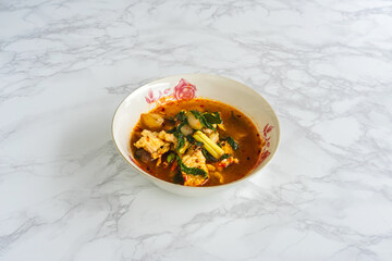 Top view of hot spicy crocodiles soup in white bowl on marble background. Spicy Thai tom yum soup  from THAI cuisine. Crocodile meat with vegetables Ingredients hot soup. Traditional asian soup.