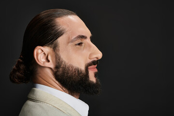 side view, portrait of bearded and confident arabic man in white shirt posing on black backdrop