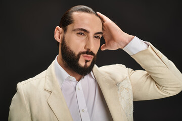 elegant and bearded arabic man in white shirt and blazer looking away on black background