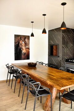 interior de area gourmet cozinha com mesa rustica de madeira, cadeiras pretas curvadas, churrasqueira moderna de porcelanato preto com cozinha cinza moderna, quadro de cavalo na parede