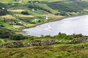 Old dry stone wall with Uig bay and houses in the background. Isle of Skye, Scottish Highlands.