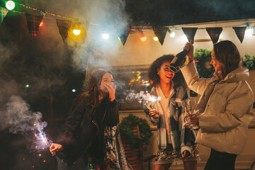 Happy smiling girls have fun together with Bengal lights sparklers near Xmas camper trailer outdoor