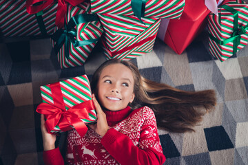 Top view photo of dreamy curious little lady dressed red print pullover lying floor guessing inside x-mas christmas gift indoors home room