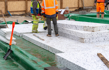 Builder placing polystyrene insulation boards on waterproofing membrane during floor construction. Energy saving concept - obrazy, fototapety, plakaty