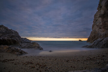 Punta Crena, bay in Liguria, shot without swimmers on a summer evening while the sun sets behind a veil of clouds. Sunset over the sea, long exposures. Varigotti, Liguria, Italy.