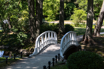 A little romantic bridge in a city park made of wood, painted in white. Park in natural light, on a sunny summer day.