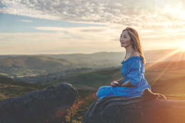 Fototapeta premium asian woman in a blue dress and a hat with a lavender bouquet in her hands on a top of mountain at summer sunset