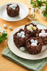 Easter chocolate nest cake with mini chocolate candy eggs with blossoming cherry or apple flowers on yellow background table. Creative recipe for Easter table with holiday decorations. Top view.