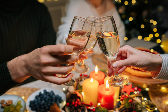 Close-up hands shot of unrecognizable happy gathering family clinking glasses with champagne, celebrating xmas, new year or birthday party, sitting at holiday dinner table with candles