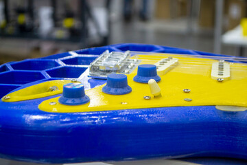 Musical instrument guitar 3D printed from molten plastic in yellow and blue colors. Part of guitar...