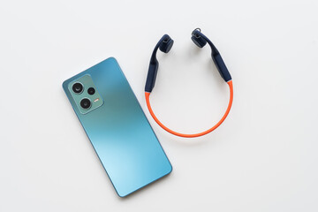 Wireless Waterproof Bone Conduction Headphones with blue smartphone on a white background. Open ear design. Navy orange headphones.