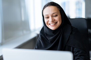 Beautiful woman with abaya dress working on her computer. Middle aged female employee at work in a business office in Dubai. Concept about middle eastern cultures and lifestyle