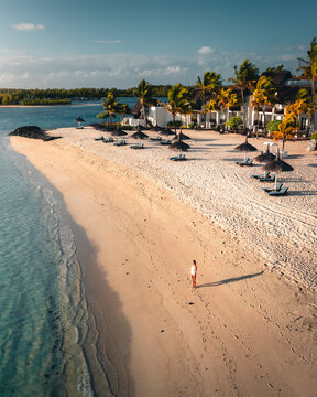 Aerial view of a woman on the beach along the shore with umbrellas at sunset, Ilot Lievres, Trou d'Eau Douce, Flacq district, Mauritius.