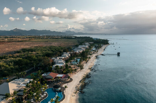 Aerial view of hotels and resorts on the beachfront along the coastline facing the ocean at sunset in Pointe aux Piments, Pamplemousses, Mauritius.