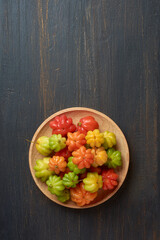 surinam cherries, eugenia uniflora, aka pitanga, brazilian or cayenne cherry, vibrant colorful fruits on wooden plate, isolated on black rustic background surface with copy space
