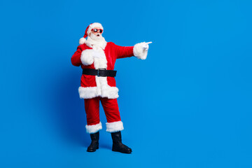 Full body photo of retired old man white beard point empty space wear trendy santa claus costume coat isolated on blue color background