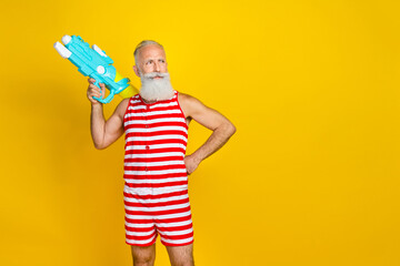 Concept of pool party old gray bearded man in swimsuit holding water gun ready for battle look...