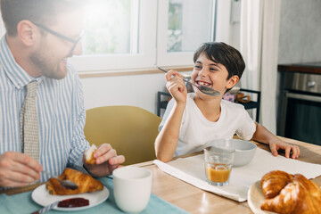 Son is having breakfast wit his father in the morning.