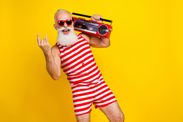 Photo of crazy brutal grandfather wearing striped red swimsuit show rocker metal sign with boombox isolated on yellow color background
