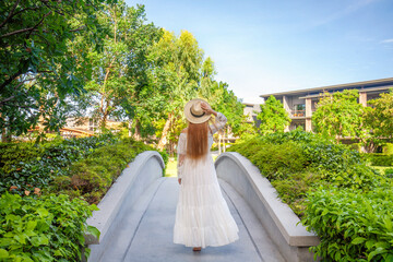Woman in elegant white dress strolls through modern Thai hotel, immersed in lush greenery. Thailand vacation bliss. - Powered by Adobe