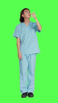 Front view of asian medical nurse checks hologram in studio with greenscreen design, working with holographic icon tab and artificial intelligence. Male specialist in uniform with healthcare expertise