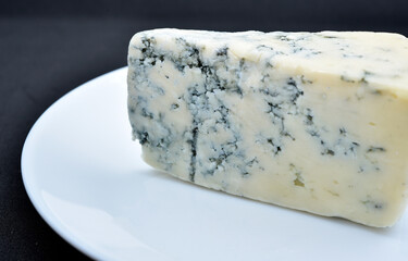 A piece of cheese with blue mold on a white plate. Delicious cheese.