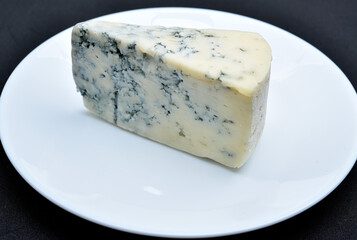 A piece of cheese with blue mold on a white plate. Delicious cheese.