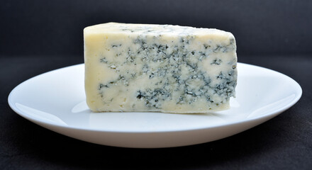 A piece of cheese with blue mold on a white plate. Delicious cheese.