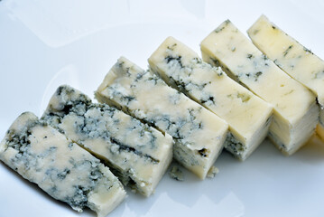 Sliced cheese with blue mold on a white plate. Delicious breakfast with cheese.