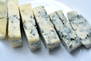 Sliced cheese with blue mold on a white plate. Delicious breakfast with cheese.