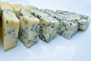 Sliced cheese with blue mold on a white plate. Delicious breakfast with cheese.