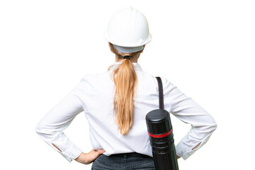 Young architect caucasian woman with helmet and holding blueprints over isolated background in back...
