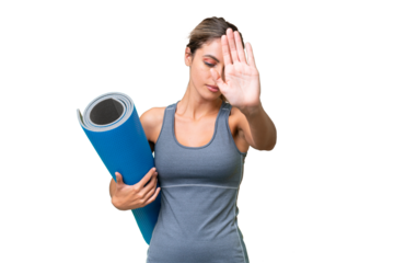 Pretty Young Uruguayan sport woman going to yoga classes while holding a mat over isolated background making stop gesture and disappointed