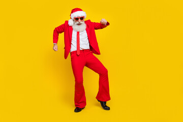 Fototapeta na wymiar Full length photo of good mood man pensioner dressed red suit santa hat dancing empty space isolated yellow color background