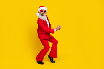 Fototapeta na wymiar Full length photo of attractive lucky retired guy wear red tux claus hat having fun rising fist isolated yellow color background