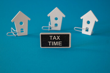 Wooden houses sits next to a wooden black board with the word Tax Time. beautiful blue background....