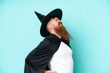 Young wizard in halloween isolated on blue background suffering from backache for having made an...