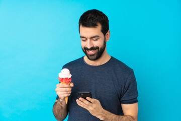 Young man with a cornet ice cream over isolated blue background sending a message with the mobile