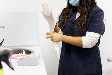 An unrecognizable woman in a medical uniform puts on latex gloves before starting work. Hygiene...