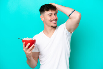 Young caucasian man holding a bowl of cereals isolated on blue background has realized something...