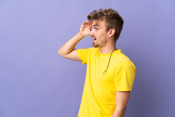 Young handsome blonde man isolated on purple background with surprise expression while looking side