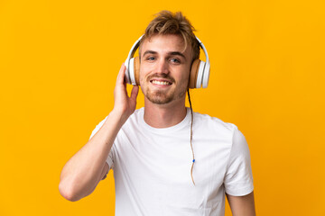 Young handsome blonde man isolated on yellow background listening music
