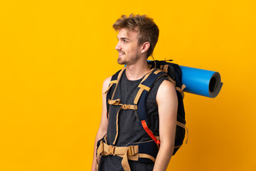 Young mountaineer man with a big backpack isolated on yellow background looking to the side and...