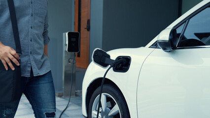 A man unplugs the electric vehicle's charger at his residence. Concept of the use of electric...